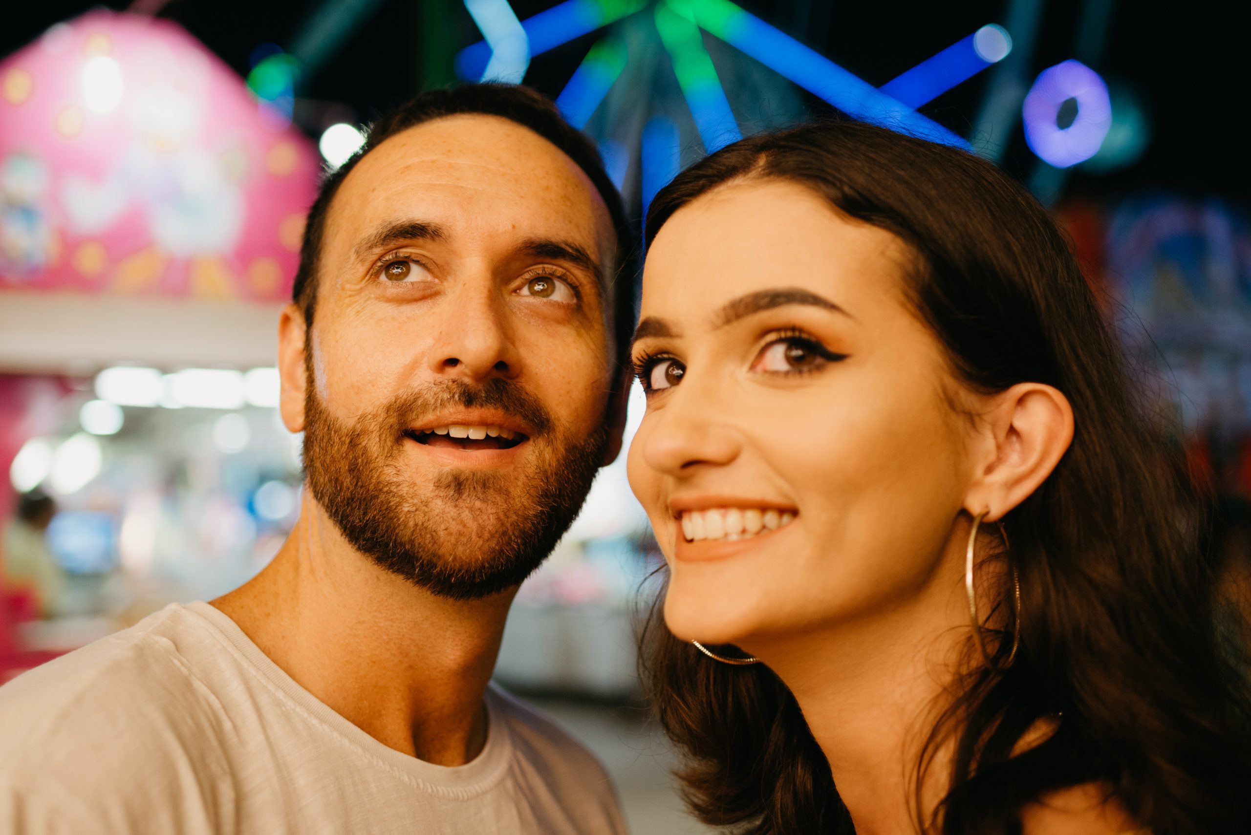 Why Qualifying Women Boosts Attraction - And How To Do It Naturally 24 Why Qualifying Women Boosts Attraction - A Close Portrait Of A Woman In A Yellow Dress With A Plunging Neckline Who Is Smiling With Her Boyfriend With A Beard Near Amusement Rides. A Couple Of Lovers On A Date At The Fair In Valencia