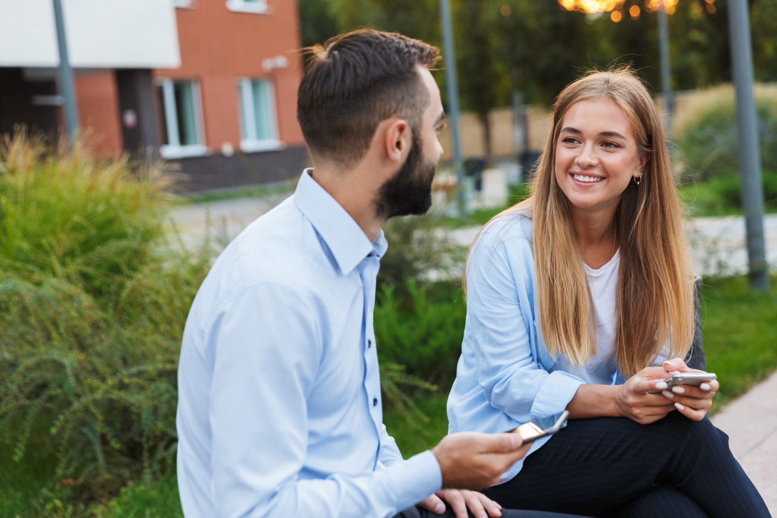 How To Friend Zone A Girl (Without Ruining The Vibe Or Losing Power) 14 How To Friend Zone A Girl - Photo Of A Young Cheery Man And Woman Businesspeople Sit Outside At The Street Using Mobile Phones Talking With Each Other.