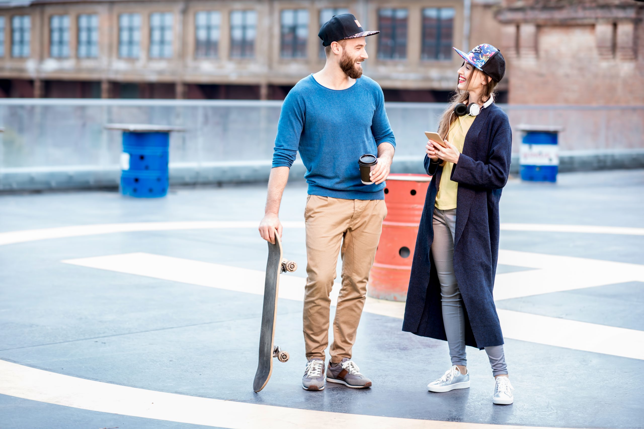 How To Get A Woman’s Attention Using Intrigue (Without Being Obvious) 28 Get A Woman’s Attention Using Intrigue - Stylish Couple In Blue Sweaters And Caps Talking Together Standing With Skateboard Outdoors On The Rooftop Playground