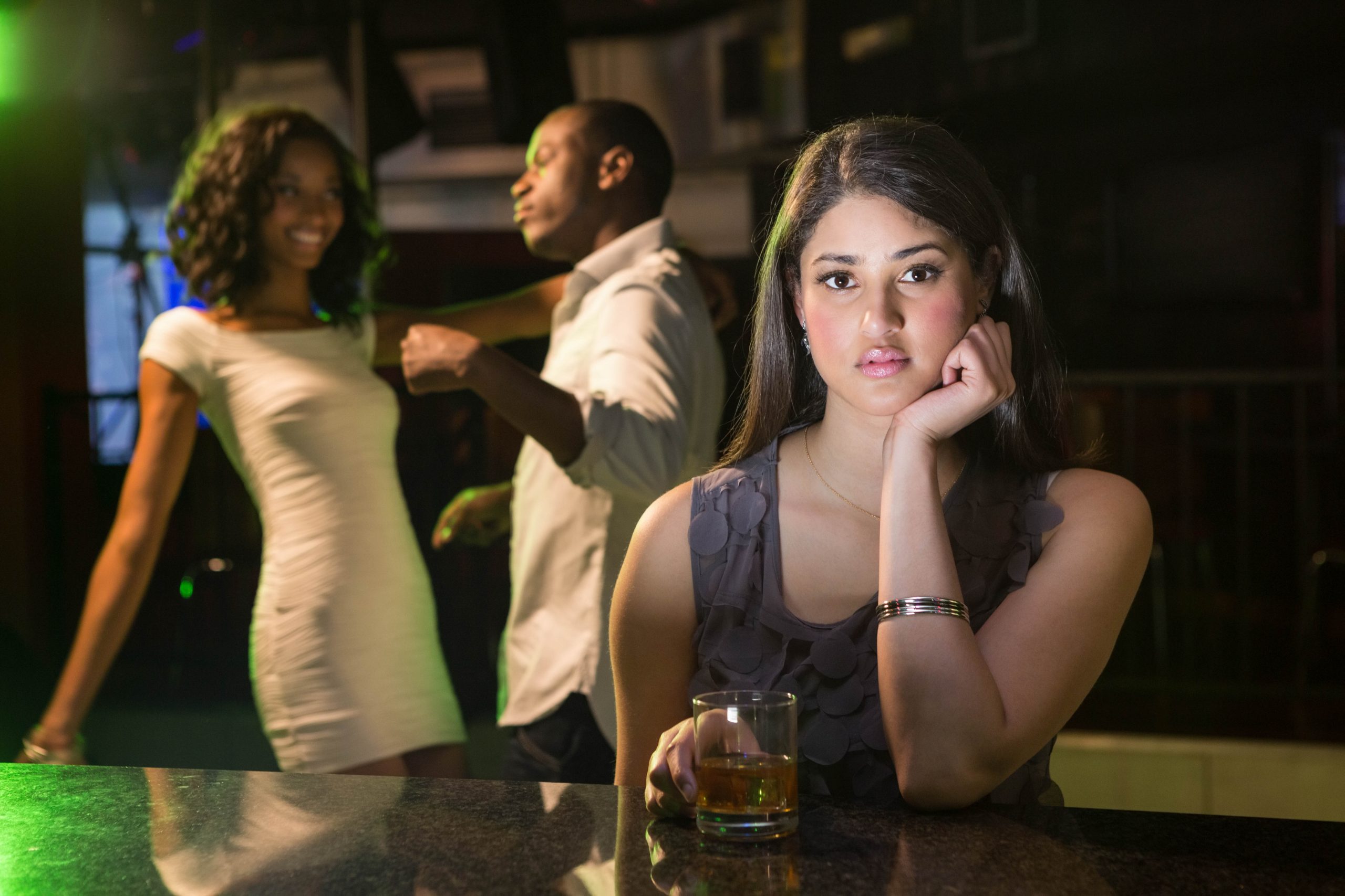 Why Ignoring A Woman Works (And Why It’s Dangerously Addictive) 24 Why Ignoring A Woman Works - Unhappy Woman Sitting At Bar Counter And Couple Dancing Behind Her In Bar