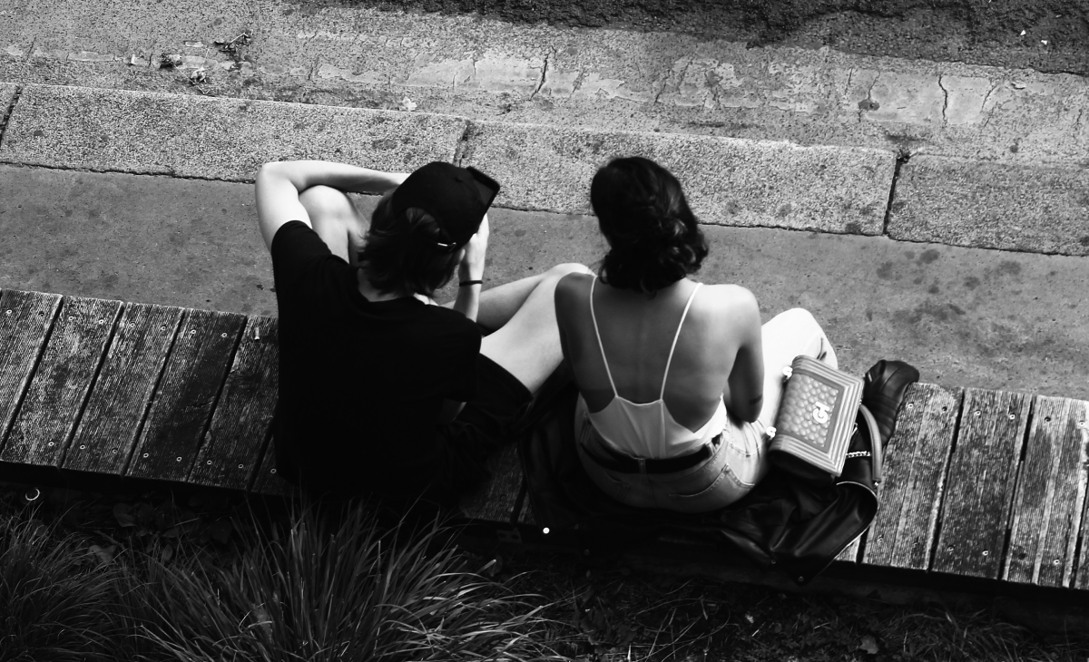 A man and a woman sitting closely on a wooden bench, engaging in deep conversation, subtly building sexual tension through body language and eye contact